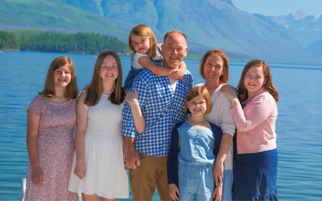 a picture of a family with five girls in front of a lake and mountains.